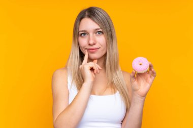 Soyutlanmış mavi arka planı olan genç sarışın kadın elinde donut tutuyor.