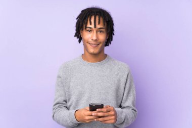 Genç Afrikalı Amerikalı, mor arka planda izole edilmiş cep telefonuyla bir mesaj gönderiyor.