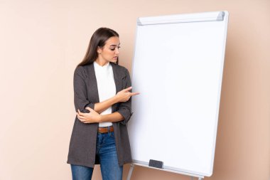 Beyaz tahtada sunum yapan genç bir kadın beyaz tahtada sunum yapıyor ve onu işaret ediyor.