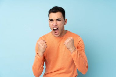 Kafkasyalı yakışıklı adam mavi arka planda izole edilmiş. Kötü bir durum yüzünden hayal kırıklığına uğramış.