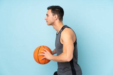 İzole edilmiş mavi arka planda basketbol oynayan adam.