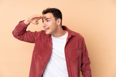 Beyaz tenli yakışıklı adam bej arka planda izole edilmiş. Bir şeye bakmak için uzaklara bakıyor.