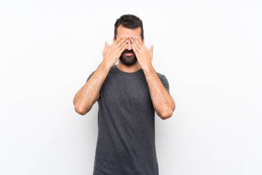 İzole edilmiş beyaz arka planda genç yakışıklı adam gözlerini elleriyle kapatıyor.