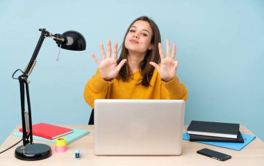 Öğrenci kız, mavi arka planda izole bir şekilde evinde ders çalışıyor. Parmaklarıyla dokuzunu sayıyor.