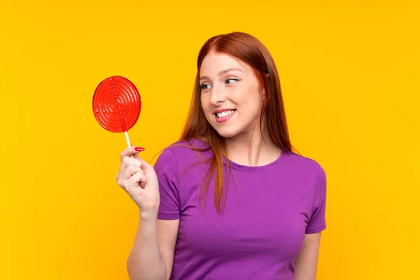 Jovem ruiva segurando um pirulito sobre fundo amarelo — Fotografia de Stock