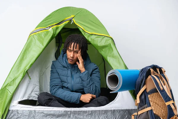 Young african american man inside a camping green tent with headache