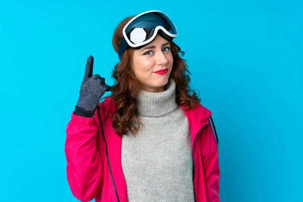 一个滑雪场的女人 戴着雪板眼镜 越过孤立的蓝色墙壁 用食指指尖指尖 这真是个好主意 — 图库照片