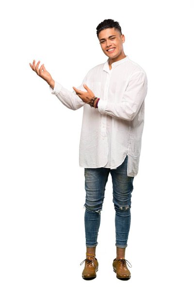 A full-length shot of a Young man extending hands to the side for inviting to come over isolated white background
