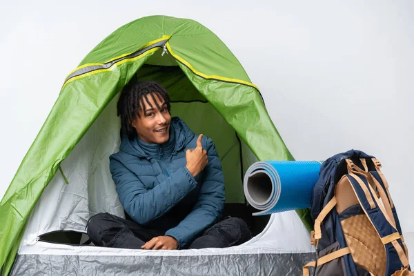 Young african american man inside a camping green tent pointing back