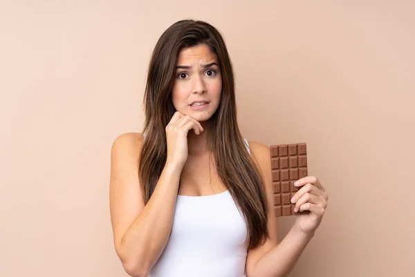 Teenager Dívka Přes Izolované Pozadí Čokoládovou Tabletu Mají Pochybnosti — Stock fotografie