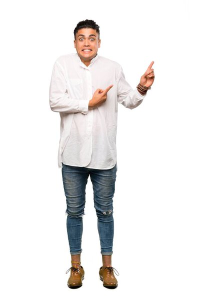 A full-length shot of a Young man frightened and pointing to the side over isolated white background