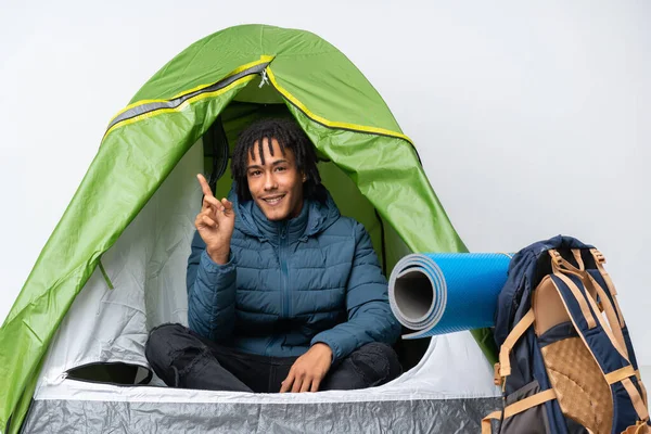 Young african american man inside a camping green tent pointing finger to the side
