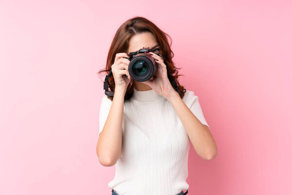 Young Russian woman over isolated pink background with a professional camera