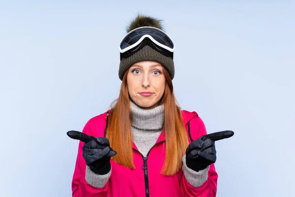 Lyžařka Zrzka Snowboardovými Brýlemi Přes Izolovanou Modrou Stěnu Ukazující Laterály — Stock fotografie