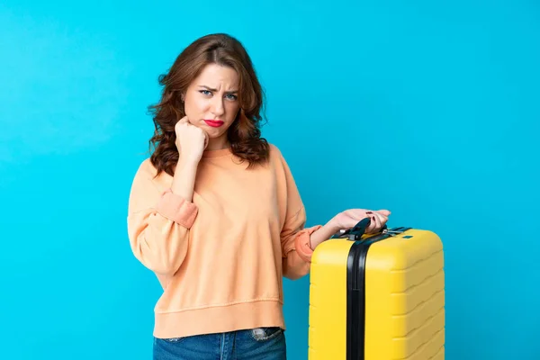 Traveler woman with suitcase over isolated blue background unhappy and frustrated