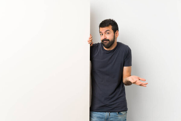 Young handsome man with beard holding a big empty placard making doubts gesture
