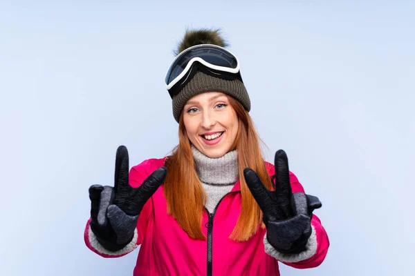 Skirennläuferin Mit Snowboardbrille Über Einsamer Blauer Wand Lächelt Und Zeigt — Stockfoto