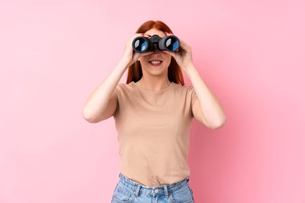 Ung Rödhårig Kvinna Över Isolerad Rosa Bakgrund Med Svart Kikare — Stockfoto