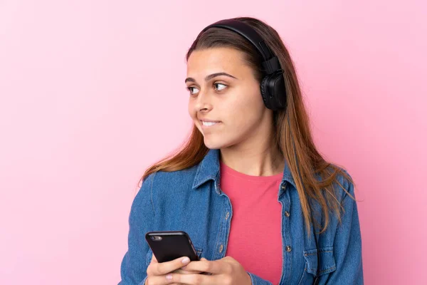 Teenager dívka poslech hudby s mobilem přes izolované růžové w — Stock fotografie