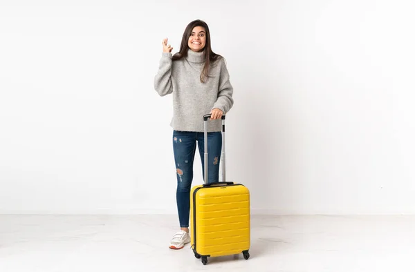 独立した白い壁の上にスーツケースを持つ旅行者の女性の完全な長さの体指が交差 — ストック写真