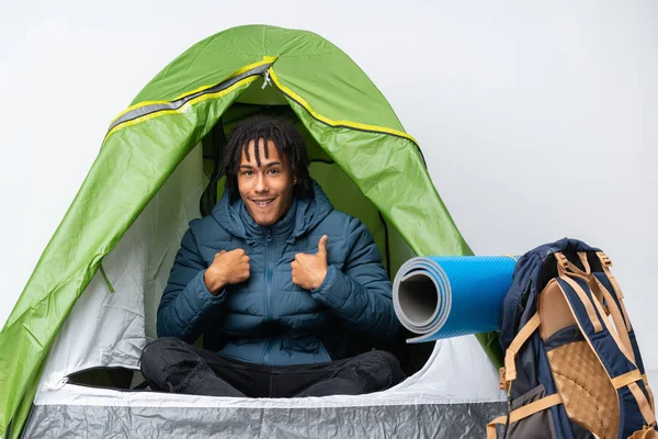 Young african american man inside a camping green tent with surprise facial expression