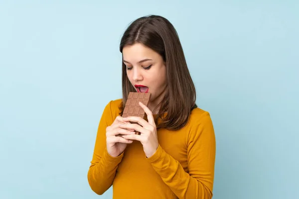 Adolescente Menina Isolado Fundo Azul Comer Comprimido Chocolate — Fotografia de Stock