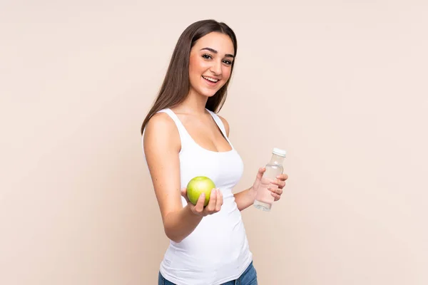 年轻的高加索女人 带着苹果和一瓶水 与米色背景隔离在一起 — 图库照片