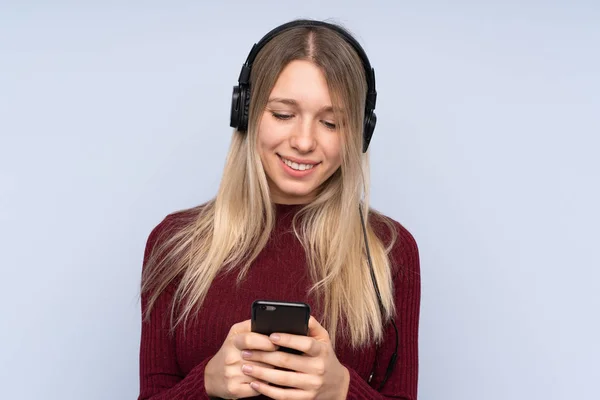 Молодая Блондинка Изолированном Синем Фоне Слушать Музыку Смотреть Мобильный — стоковое фото