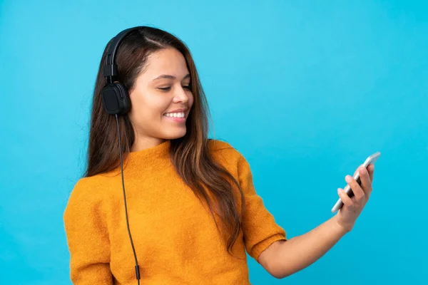 Jovem Mulher Ouvindo Música Com Celular Sobre Parede Azul Isolada — Fotografia de Stock