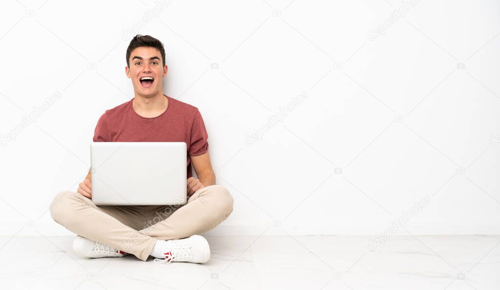 Teenager man sitting on the flor with his laptop with surprise facial expression