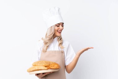 Şef üniformalı ergen kız. İzole edilmiş beyaz arkaplan üzerinde birkaç ekmek bulunan bir masayı tutan kadın fırıncı, avuç içi hayali bir kopyacı tutuyor.