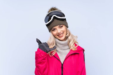 Snowboard gözlüklü kayakçı kız izole edilmiş mavi arka planda telefon jesti yapıyor.