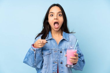 Izole mavi arka plan üzerinde çilek milkshake ile genç kadın şaşırttı ve ön işaret