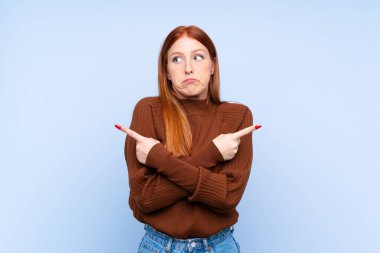 İzole edilmiş mavi arka planı olan genç kızıl saçlı kadın, yandakilerin şüpheleri olduğunu gösteriyor.
