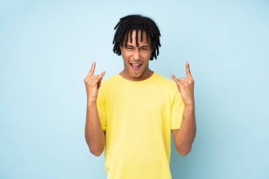 Genç Afrikalı Amerikalı adam mavi arka planda izole edilmiş kaya jestleri yapıyor.