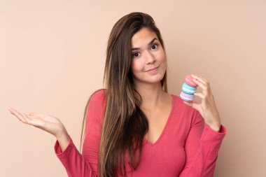 Soyutlanmış arka plan üzerinde genç bir kız renkli Fransız kurabiyeleri tutuyor ve şüpheli hareketler yapıyor.