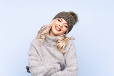Kışlık şapkalı genç kız mavi arka planda gülüyor.