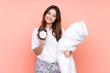 Pijamalı genç bir kadın ve elinde pembe arka planda izole edilmiş klasik bir saat var.