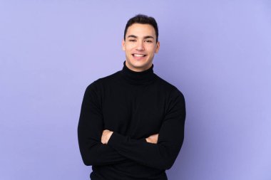 Balıkçı yaka kazaklı genç beyaz adam mor arka planda izole edilmiş kollarını ön tarafta çapraz tutuyor.