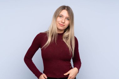 Soyutlanmış mavi arka planda genç sarışın kadın gülüyor.