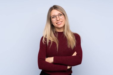 Gözlüklü ve gülümseyen, soyutlanmış mavi arka planı olan genç sarışın kadın.