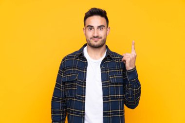 İşaret parmağı ile işaret izole sarı arka plan üzerinde genç yakışıklı adam harika bir fikir