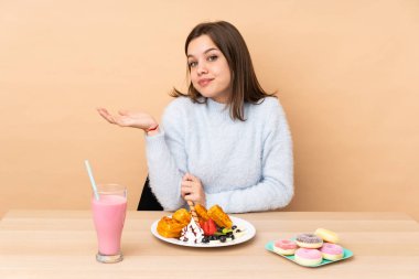 Bej arka planda izole edilmiş waffle yiyen genç kız gülümsüyor.