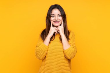 Sarı arka planda izole edilmiş genç beyaz kadın mutlu ve hoş bir ifadeyle gülümsüyor.