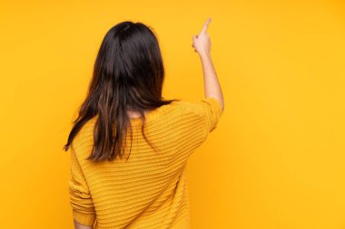 Sarı arka planda izole edilmiş genç beyaz kadın işaret parmağıyla işaret ediyor.