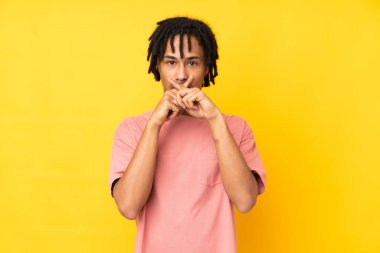 Sarı arka planda izole edilmiş genç Afro-Amerikan bir sessizlik işareti gösteriyor.
