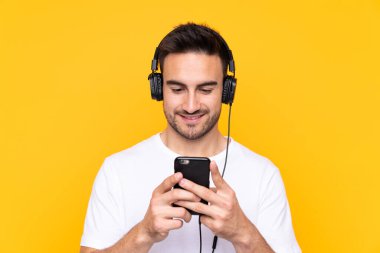 Sarı arka plandaki genç adam müzik dinliyor ve cep telefonu arıyor.