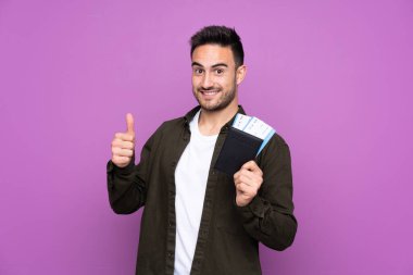 İzole edilmiş mor bir geçmişi olan genç yakışıklı bir adam. Elinde pasaport ve uçak tutuyor.