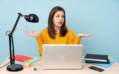 Öğrenci kız evinde çalışıyor. Mavi arka planda tek başına. Kopyalama alanını iki eliyle tutuyor.