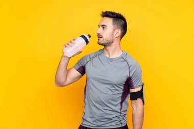 Spor adamı, izole edilmiş sarı duvarda, spor su şişesiyle.